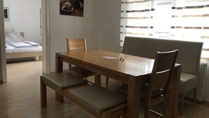 A dining area with a wooden table, four chairs, and a bench. There is a bed with a striped pillow in the background. - Appartement- Steinkirchner (Straubing)