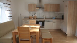 A modern kitchen with wooden cabinets, a dining table with chairs, and a built-in oven. - Appartement- Steinkirchner (Straubing)