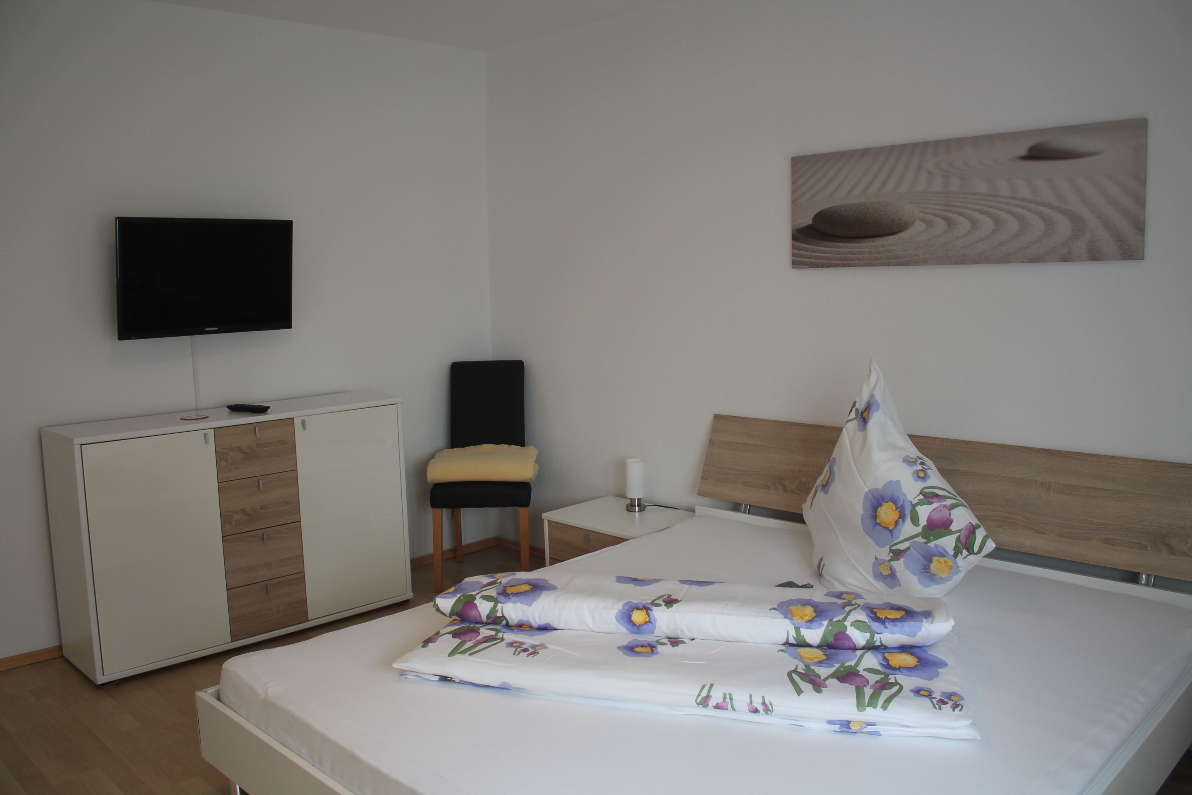 A bedroom with a bed, a wardrobe, a television, and a painting on the wall.