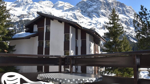 A chalet with a balcony, a round table, and white chairs.