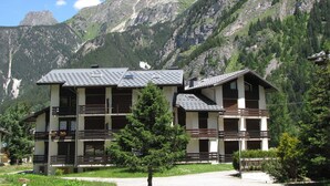 A modern building with multiple balconies, surrounded by lush greenery and mountains.