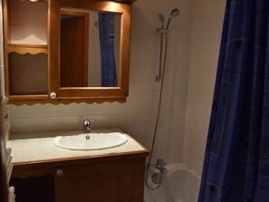 Ein Badezimmer mit einem hölzernen Waschtisch, einem weißen Waschbecken, einem Spiegel, einer Dusche und einem blauen Duschvorhang.