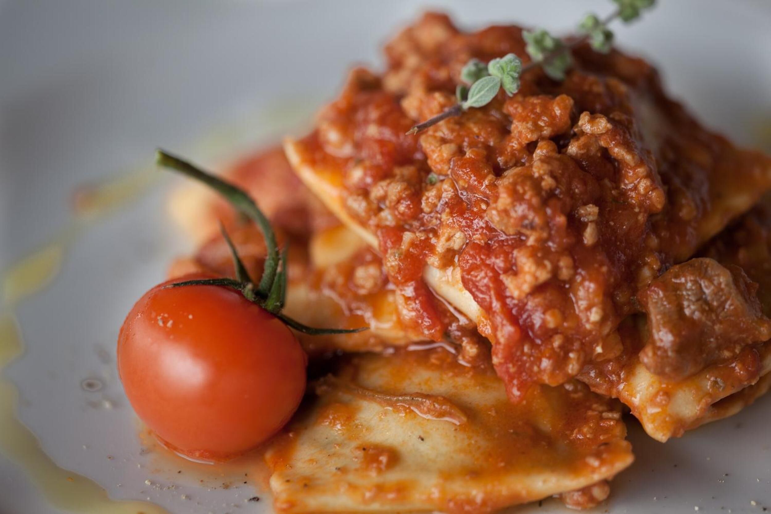 A plate of ravioli with a tomato and a sprig of herb.