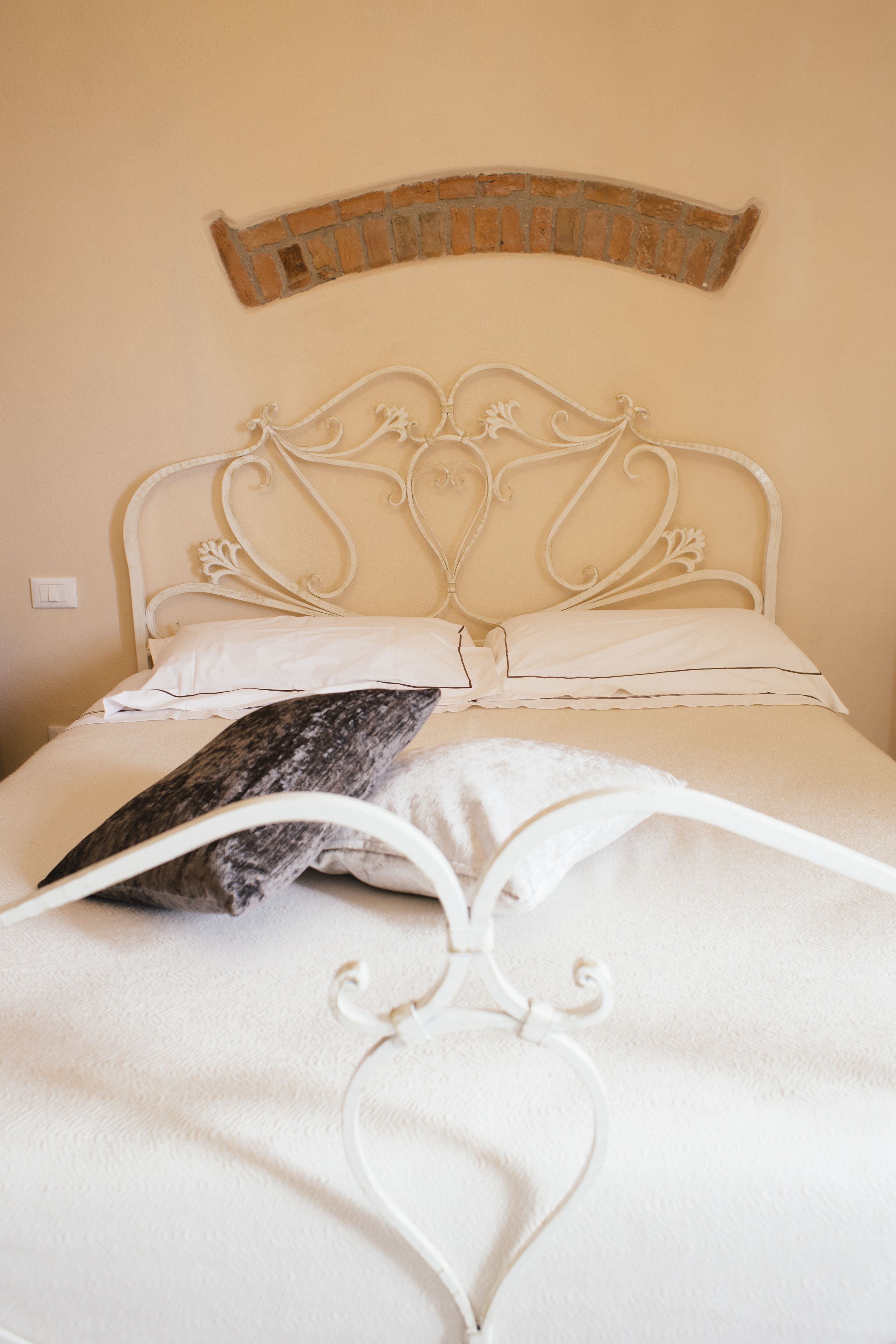 A bed with a white metal headboard, white bedding, and a decorative brick wall above.