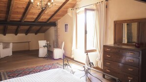 Een slaapkamer met een houten plafond, een bed, een dressoir, een stoel en een raam met gordijnen.
