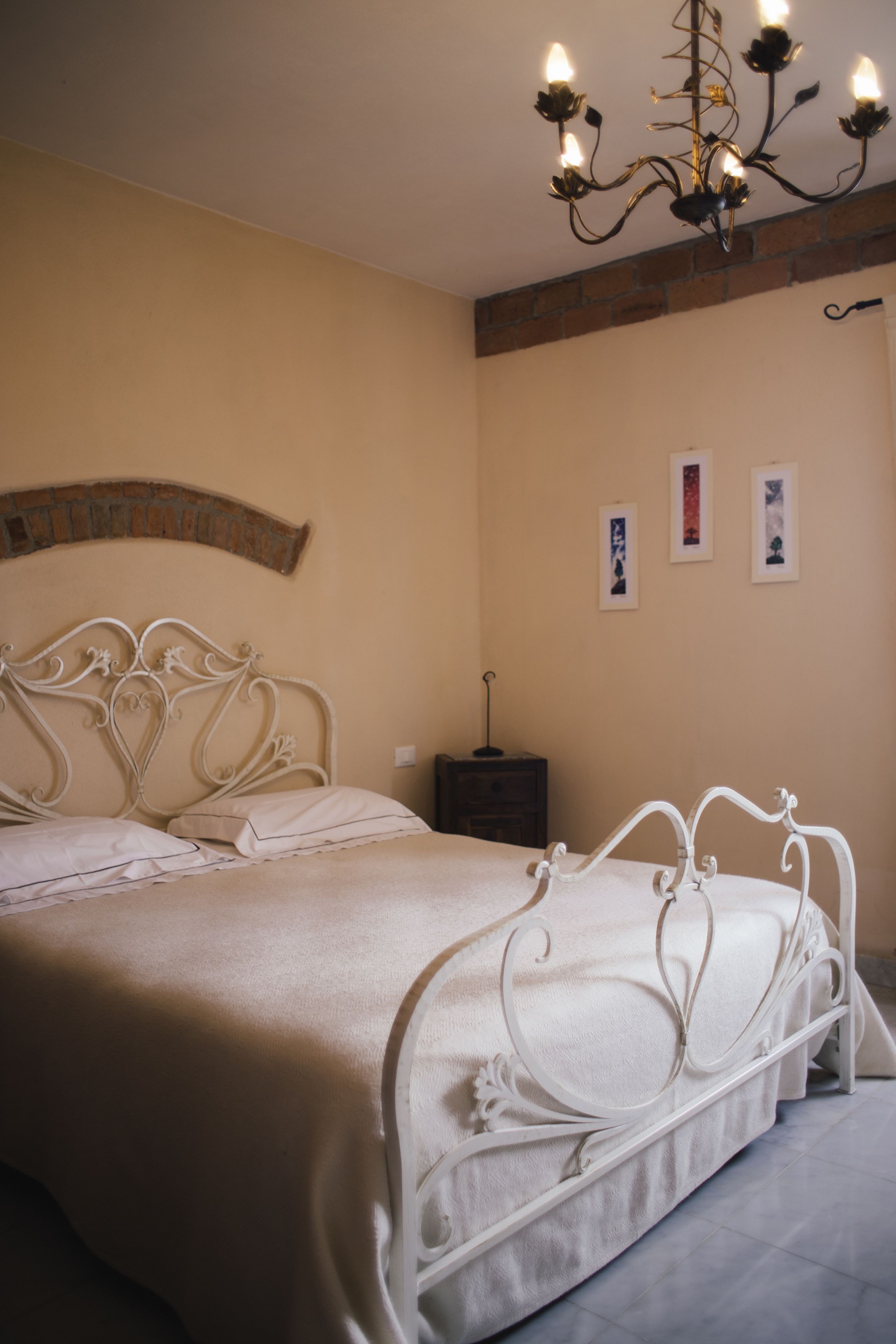Une chambre à coucher avec un lit en métal blanc, un lustre et un mur en briques.