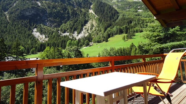 A wooden deck with a table and chairs, overlooking a mountainous landscape with green fields and trees. - Comfortable 4-room duplex, 6 pers, garage, Pralognan-la-Vanoise (Pralognan-la-Vanoise)