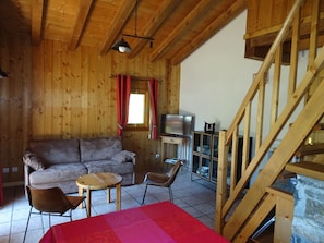 Interior em madeira com sofá, televisão, mesa e escada.