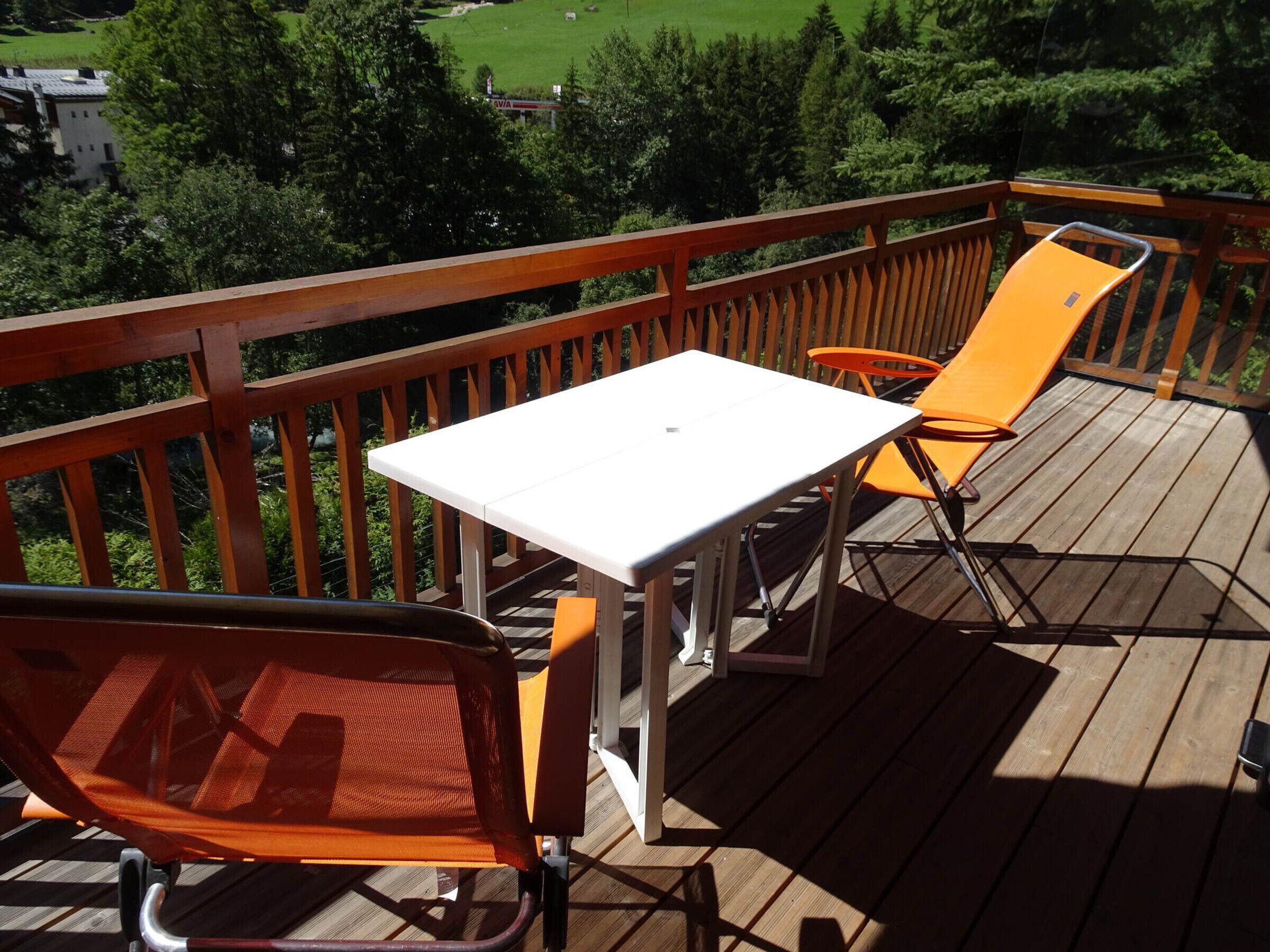 A wooden deck with a white table and orange chairs, overlooking a green landscape.