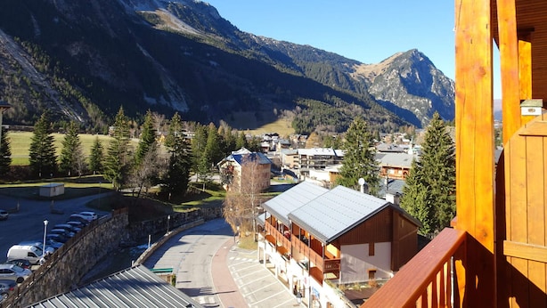 A mountain lodge with a view of the surrounding mountains, a parking area, and a stone wall. - Cozy studio near shops, south balcony (Pralognan-la-Vanoise)