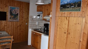 A kitchen with wooden cabinets, a microwave, a coffee maker, and a dining table with chairs. - Cozy studio near shops, south balcony (Pralognan-la-Vanoise)