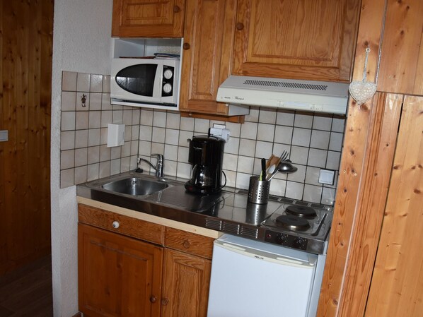 A compact kitchen with wooden cabinets, a microwave, a coffee maker, a sink, and a dishwasher.
