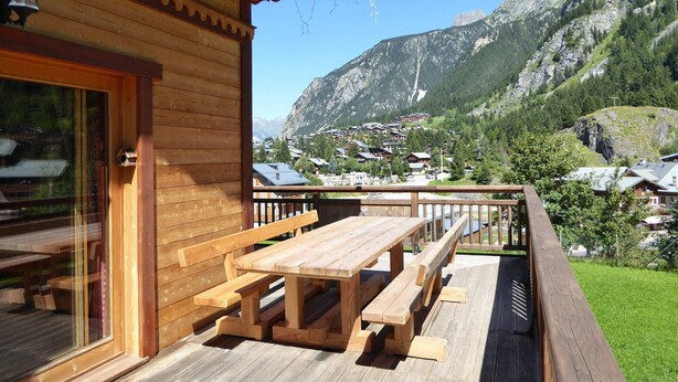 A wooden cabin with a deck and a view of a mountain village.