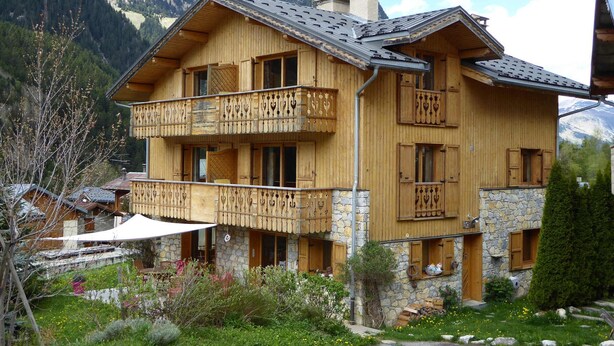 Eine Holzhütte mit Stein Fundament, Balkone mit schmiedeeisernen Geländern und einer Bergkulisse.