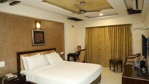 A hotel room with a large bed, a desk, a chair, a television, and a ceiling fan. - Hotel Anantha Executive Suites (Mumbai)
