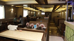 A restaurant with multiple dining tables, some with folded napkins and menus, and a few people dining. - Hotel Anantha Executive Suites (Mumbai)