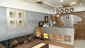 A hotel reception area with a sofa, a reception desk, and a wall-mounted clock. - Hotel Anantha Executive Suites (Mumbai)