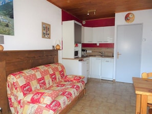 Um quarto aconchegante com cabeceira de madeira, sofá acolchoado, uma pequena mesa, cozinha com armários brancos e uma parede com detalhes em vermelho.