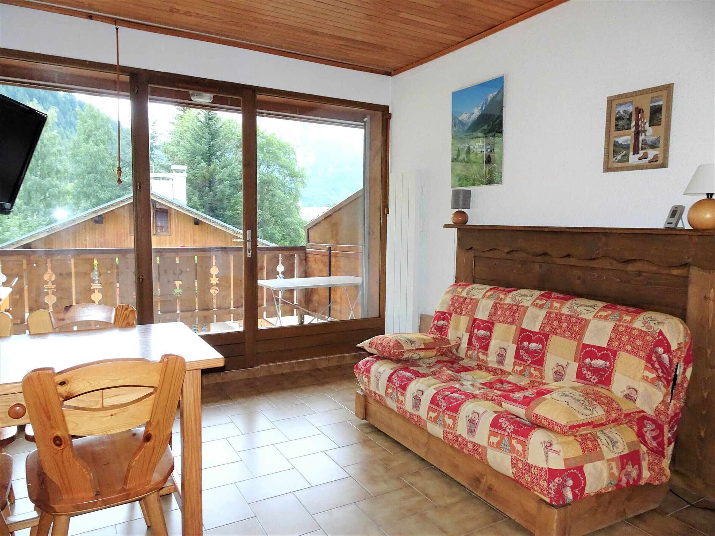 Una habitación acogedora con un sofá de madera, una mesa de comedor de madera con sillas y un ventanal que ofrece vistas a una cabaña de madera y árboles.