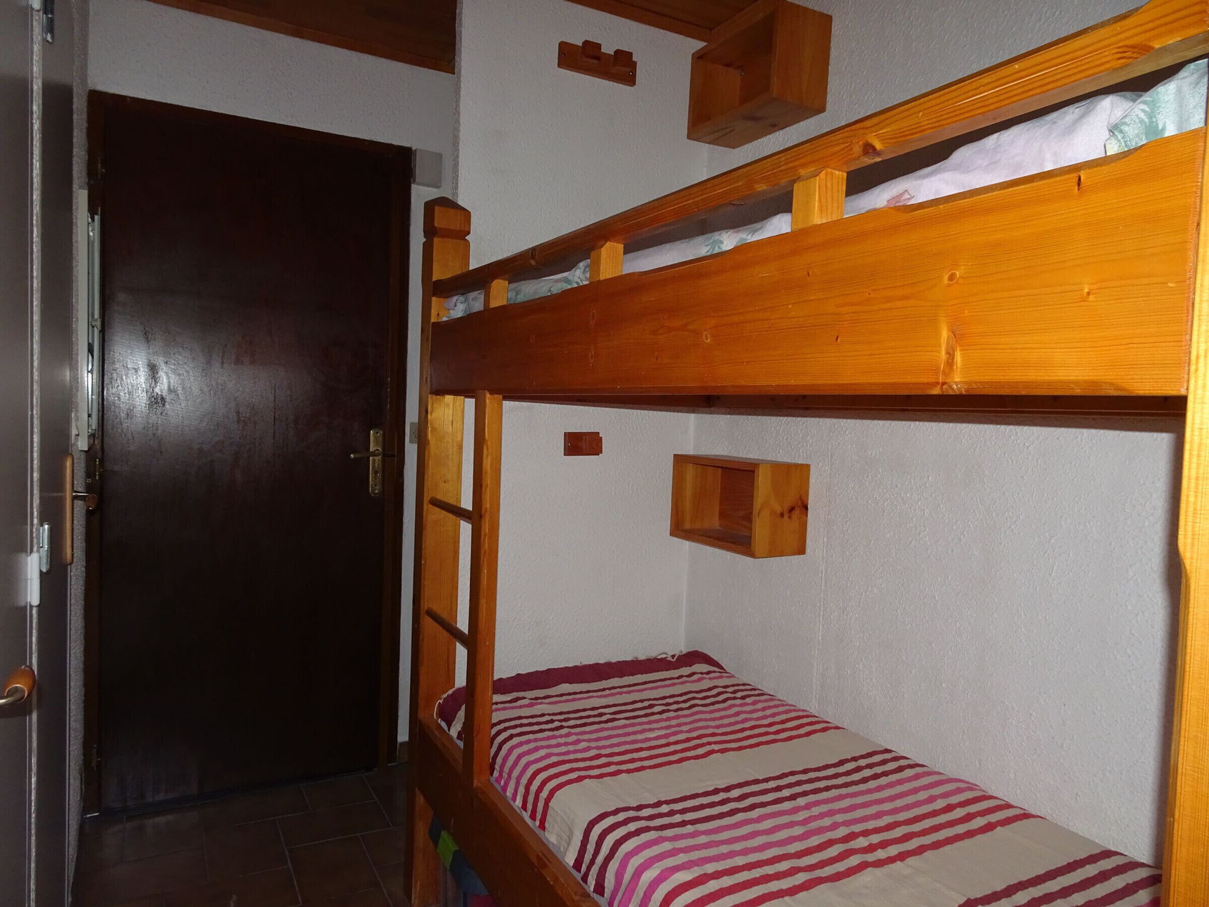 Un lit superposé avec une couverture à rayures, une étagère en bois et une porte.