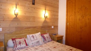 A wooden-paneled bedroom with a bed, two wall-mounted lights, and a wooden door. - Comfortable T3 with large balcony - Pets allowed (Pralognan-la-Vanoise)