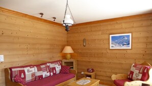 A cozy room with wooden walls, a sofa, a chair, a small table, and a lamp. - Comfortable T3 with large balcony - Pets allowed (Pralognan-la-Vanoise)
