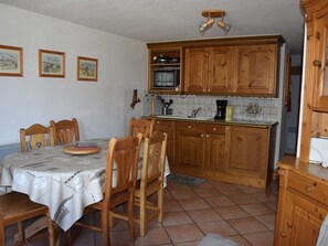 A kitchen with wooden cabinets, a dining table with chairs, a microwave, and a coffee maker. - Duplex Mezzanine 4 Rooms, Balcony, 8 Persons (Pralognan-la-Vanoise)