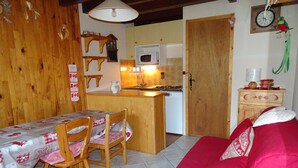 Ett mysigt rum med ett matbord och stolar i trä, en röd soffa, en köksdel med mikrovågsugn och ett träskåp.