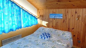 Ett rum med träpanel på väggarna, en säng, ett fönster med blå gardiner, en tavla som hänger på väggen och en liten värmare.