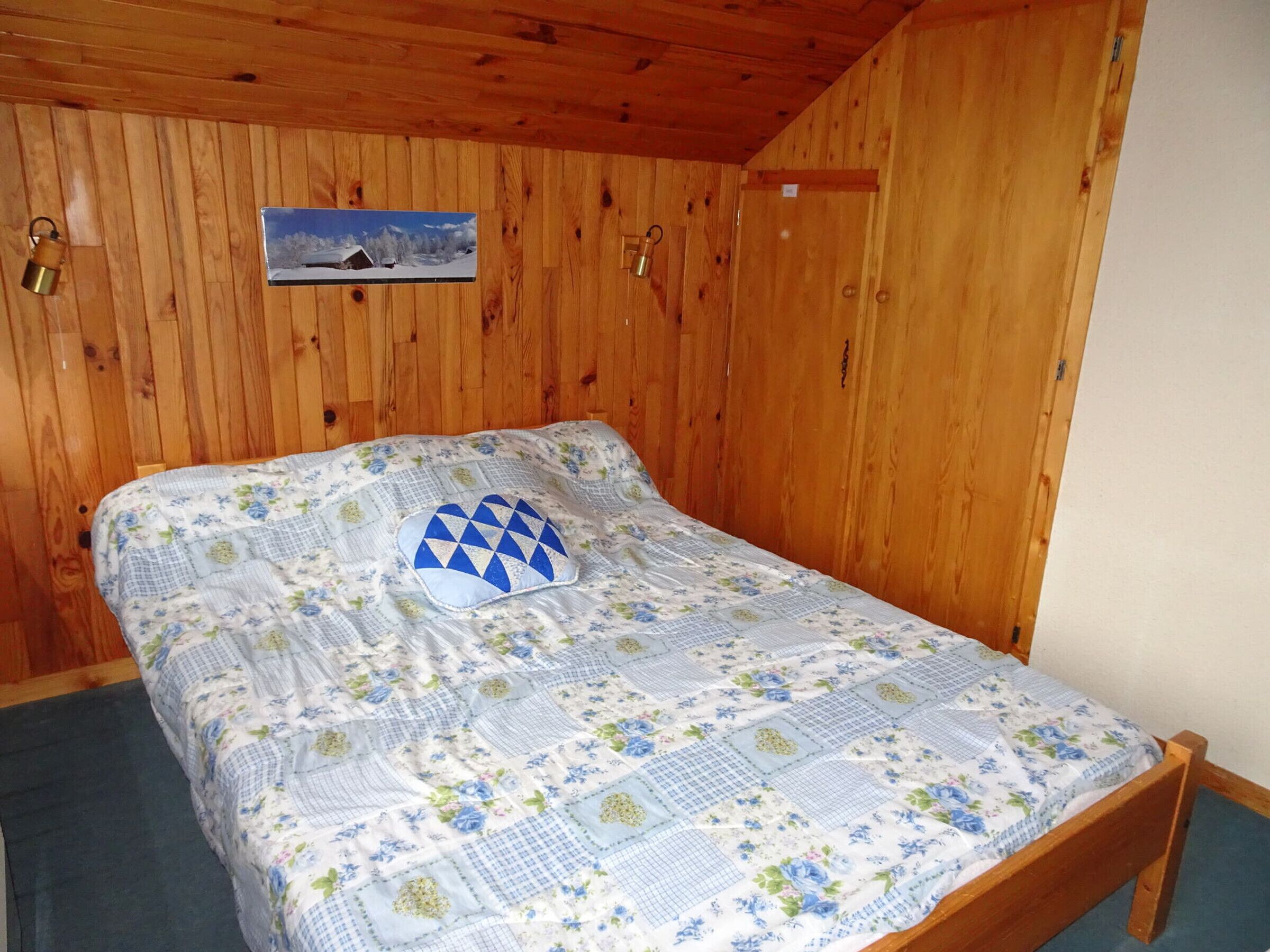Une pièce aux murs lambrés, avec un lit agrémenté d’une courtepointe à motifs floraux et d’un coussin à motifs géométriques.