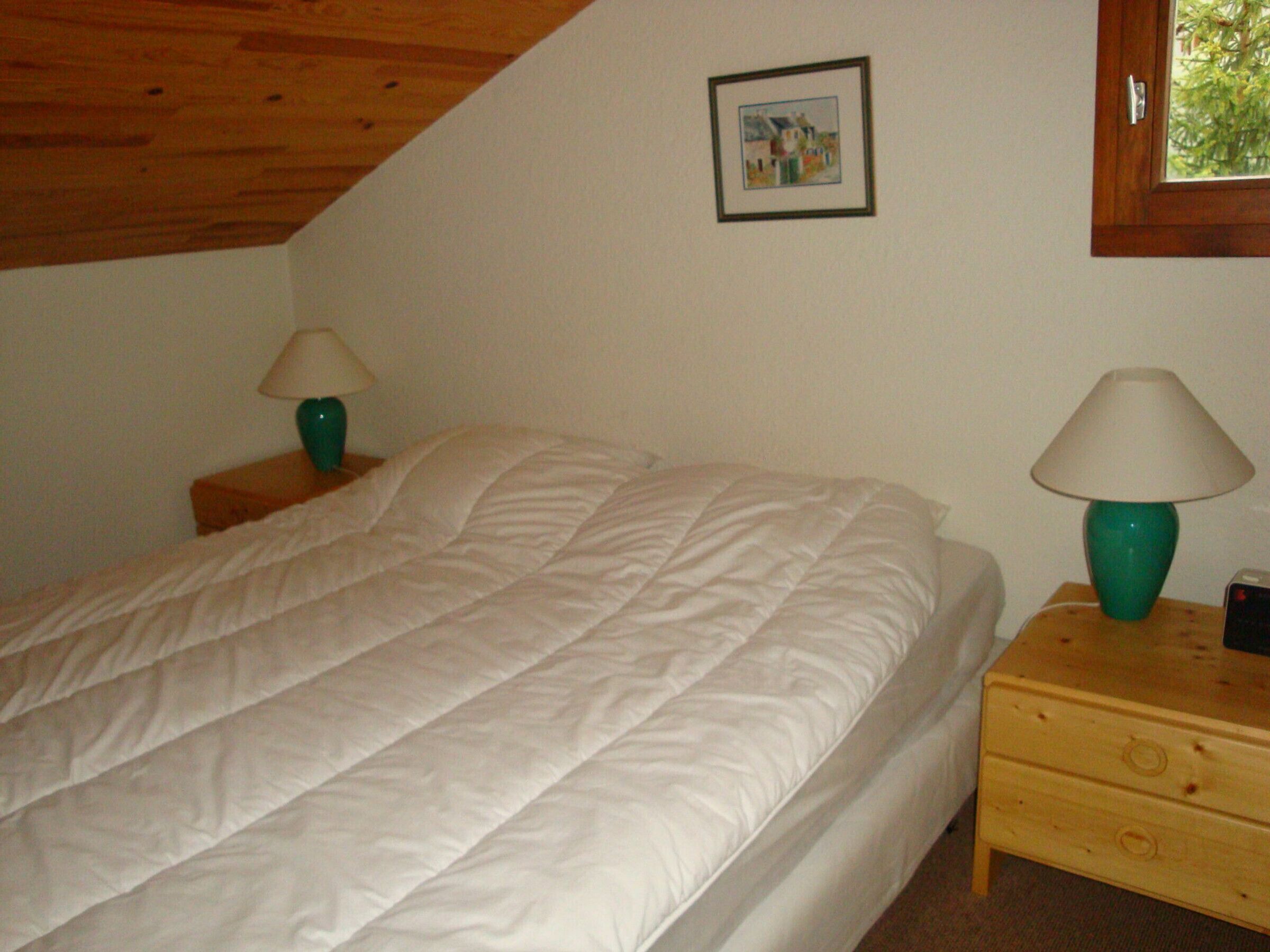 A bedroom with a bed, two nightstands, two lamps, a framed picture on the wall, and a window.