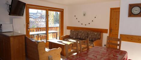 A cozy room with a wooden table, chairs, a sofa, and a TV mounted on the wall.