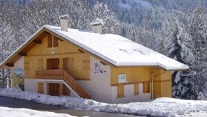 Een houten chalet met balkon, omringd door met sneeuw bedekte bomen en een berg op de achtergrond.