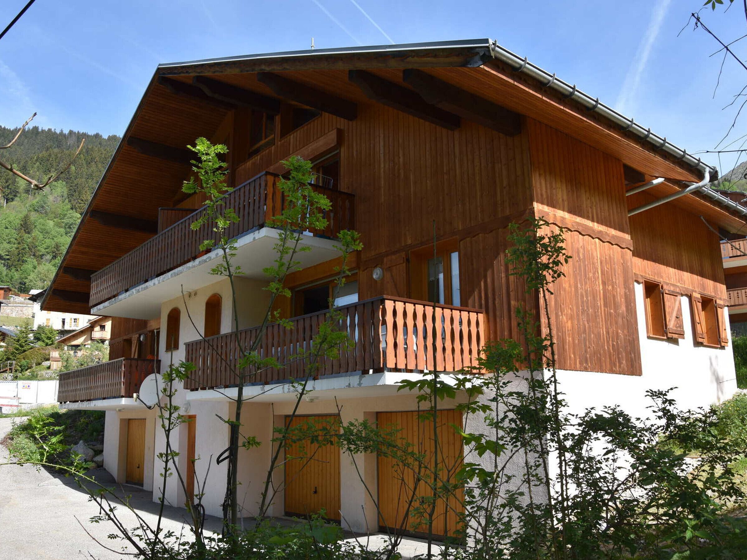 Un chalet de madera de dos pisos con un balcón en el nivel superior, rodeado de vegetación.