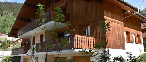Un chalet de madera de dos pisos con un balcón en el nivel superior, rodeado de vegetación.