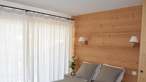 Un dormitorio con cabecera de madera, cama con ropa de cama gris, dos lámparas de noche y una mesita de noche con un reloj y un jarrón de flores.