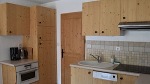 Una cocina compacta con armarios de madera, horno empotrado, lavavajillas y cafetera.