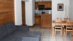 A compact living space with a kitchenette, a grey sofa, wooden dining table with chairs, and a tiled floor. - Cozy apartment with south balcony in Bozel (Bozel)