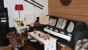 A cozy living room with a wooden wall, a black sofa, a white armchair, and a red lamp.