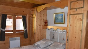 A wooden cabin bedroom with a bed, curtains, a painting, and a small shelf.