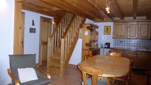 A wooden interior with a dining table, chairs, a staircase, and kitchen cabinets.
