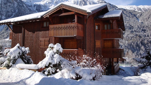 A wooden chalet with a balcony, surrounded by snow-covered mountains.