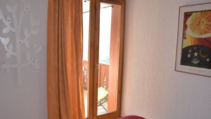A bedroom with a bed, a window with curtains, a wall with a decorative tree, and a framed picture.