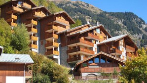 A multi-story wooden chalet with balconies, set against a mountainous backdrop.