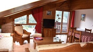 A cozy cabin interior with wooden furniture, a television, and large windows offering a view of the forest. - Spacious duplex for 6 with balcony in the Alps (Pralognan-la-Vanoise)