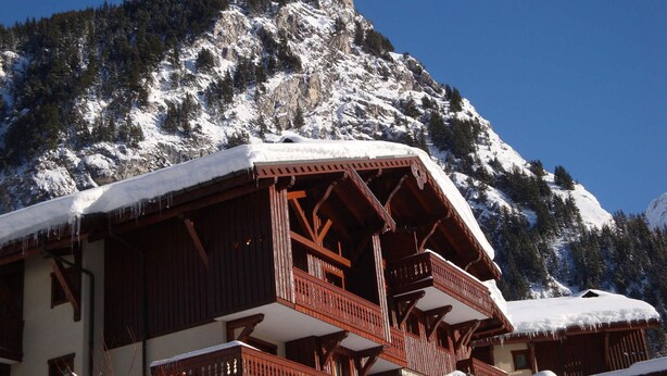 A chalet-style building with wooden balconies and a snow-covered roof, surrounded by a mountainous landscape. - Spacious duplex for 6 with balcony in the Alps (Pralognan-la-Vanoise)