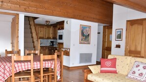 A cozy living room with a wooden dining table and chairs, a sofa with floral cushions, and a kitchen in the background. - Spacious duplex for 6 with balcony in the Alps (Pralognan-la-Vanoise)