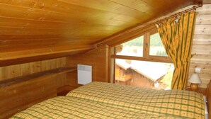 A wooden cabin room with a bed, a window with curtains, a heater, and a lamp. - Spacious duplex for 6 with balcony in the Alps (Pralognan-la-Vanoise)