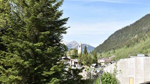 Un paysage montagneux avec un clocher d’église, une forêt dense et des immeubles d’habitation.