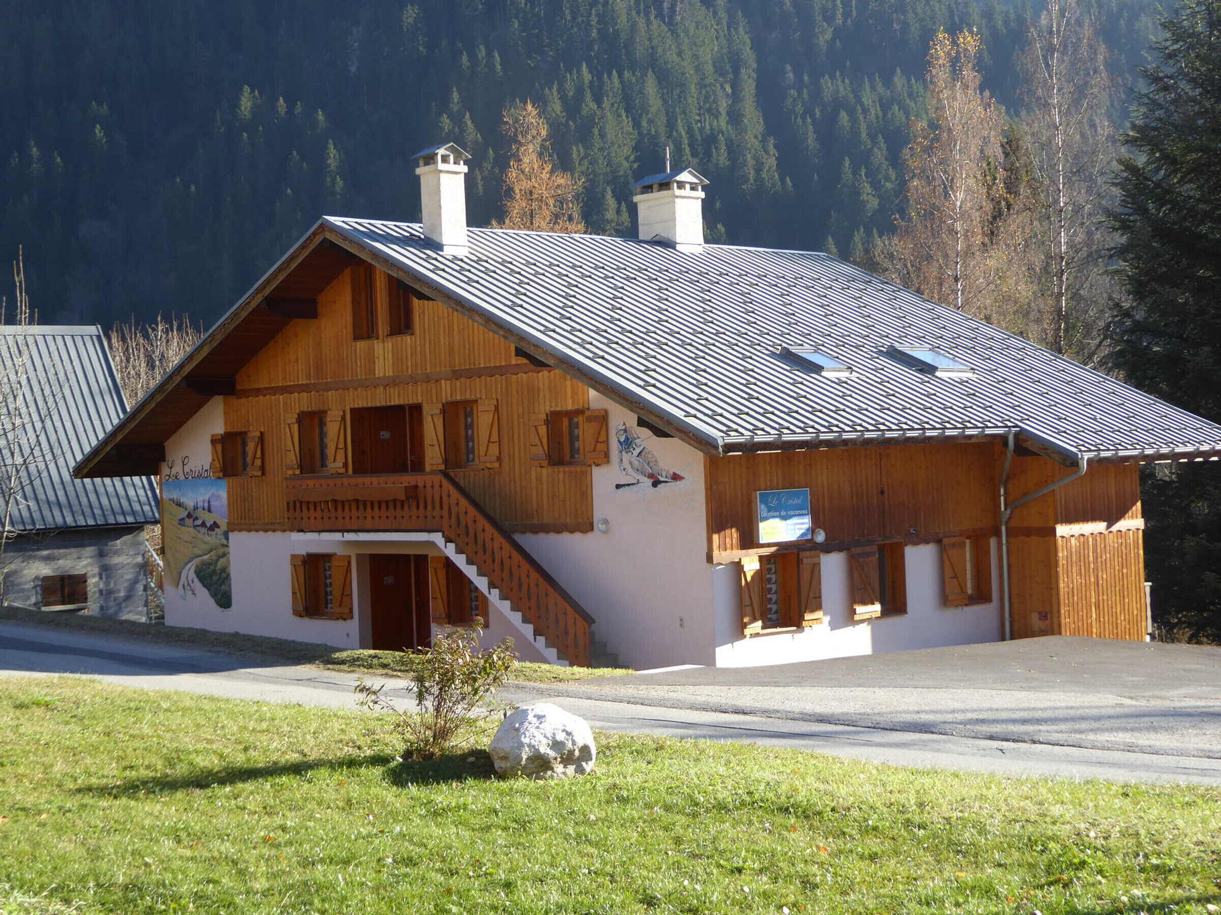 Ein zweistöckiges Holzhaus mit geneigtem Dach, einer Treppe, die zum oberen Stockwerk führt, und einem kleinen Garten mit Stein und Gras.